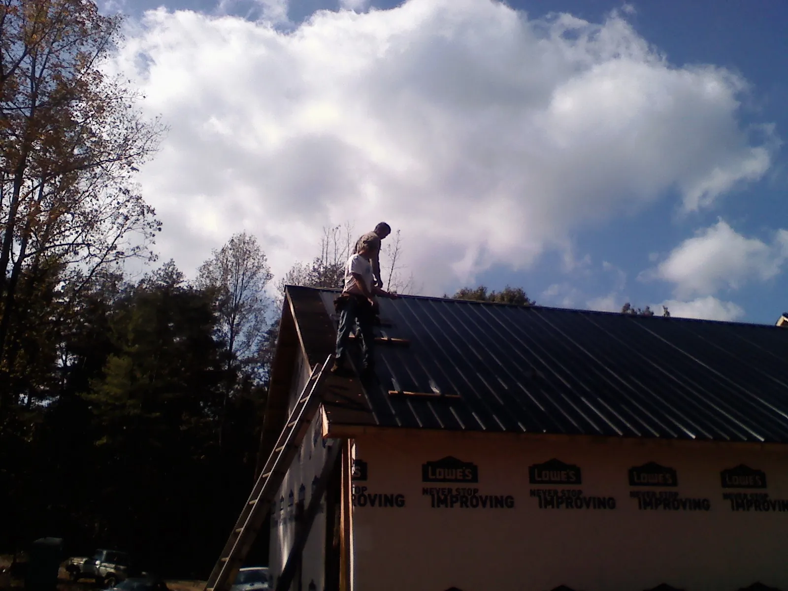 Roofer fastening dark metal panels high against a cloudy sky, from a Roof Inspection job in Boyd